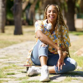 African woman with skateboard relaxing after riding skateboard listening to the music