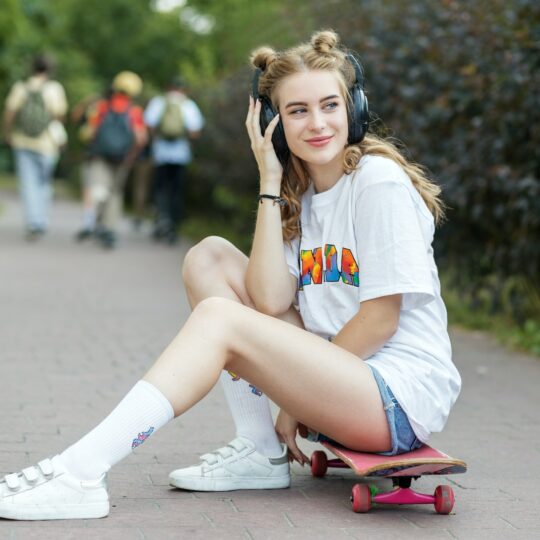 Young beautiful girl with skateboard. Listen to music on headphones. Concept of an hobby, music.